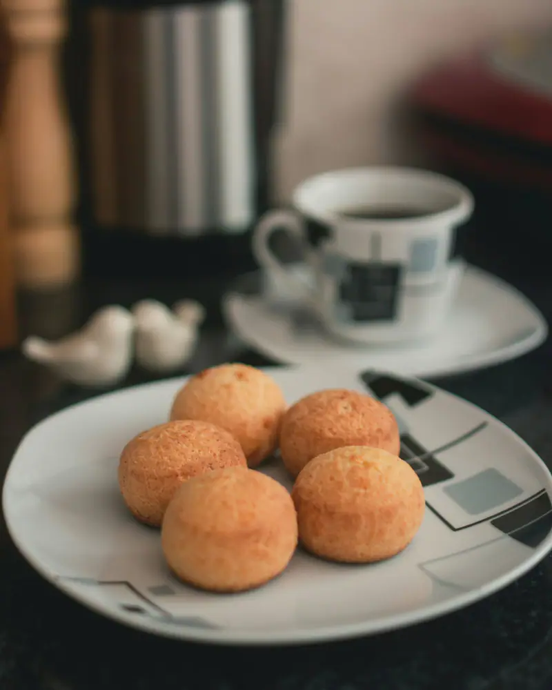 Pães de queijo num prato, com uma xícara de café ao fundo